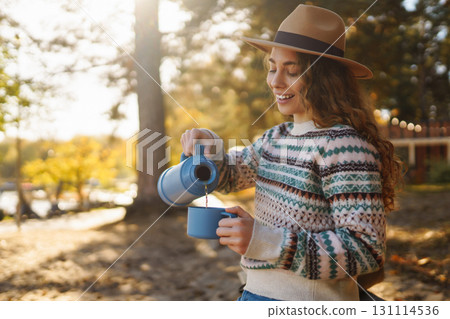 Lady drinks from thermo mug of coffee in nature. Warm up in sunny autumn forest. Travel, adventure. Lady drinks from thermo mug of coffee in nature. Warm up in sunny autumn forest. Travel, adventure. 131114536