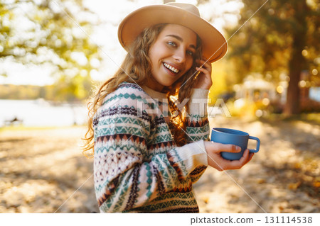 Lady drinks from thermo mug of coffee in nature. Warm up in sunny autumn forest. Travel, adventure. 131114538