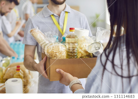 A man volunteer in a warehouse gives a woman a box of food, close-up 131114683