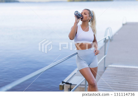 Woman Staying Hydrated During Outdoor Fitness Activity by a Scenic Waterfront 131114736