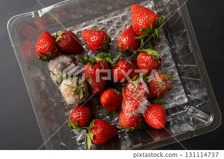 Close-up of strawberries in a plastic container, some of which are spoiled and covered with mold, symbolizing food waste, decay, and unhealthy produce. 131114737