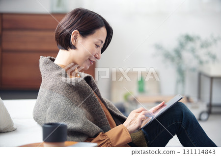 A woman in her 40s relaxing at home and looking at a tablet 131114843