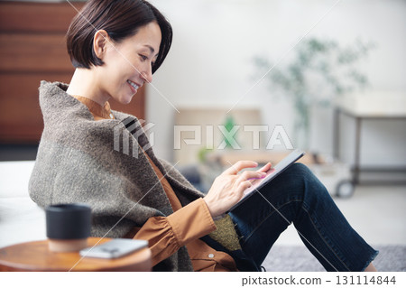一位 40 多歲的女性正在家中休息，看著平板電腦 131114844