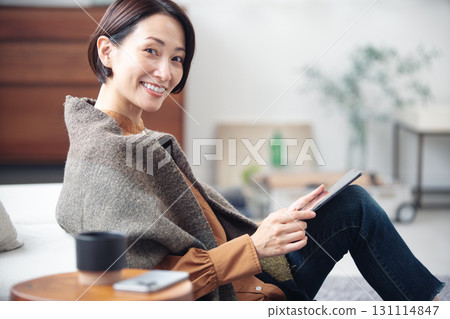 A woman in her 40s relaxing at home and looking at a tablet A woman in her 40s relaxing at home and looking at a tablet 131114847