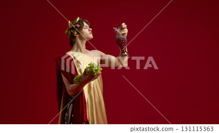 Young man in toga holding grapes and antique jug with proud look Young man in toga holding grapes and antique jug with proud look 131115363