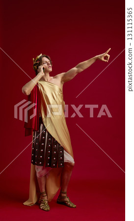 Young man in toga talking on phone with pointing gesture 131115365