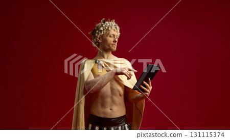 Man in Roman toga as Caesar using digital tablet with serious expression Man in Roman toga as Caesar using digital tablet with serious expression 131115374