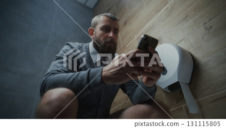 Businessman Using Smartphone, Sitting on the Toilet in Restroom Businessman Using Smartphone, Sitting on the Toilet in Restroom 131115805