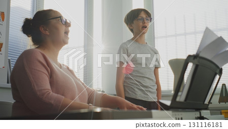 Primary School Boy Practicing Vocals During Singing Lesson. Music Teacher Playing Piano Primary School Boy Practicing Vocals During Singing Lesson. Music Teacher Playing Piano 131116181