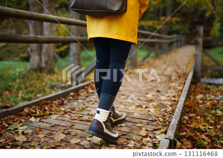 Women's feet in boots go along a wooden walking path in the autumn forest. 131116468