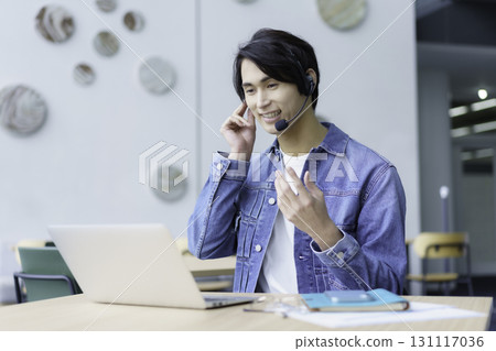 A young man wearing a headset talking on a PC in an office cafe. Photo courtesy of Sky Perfect Tokyo Media Center 131117036