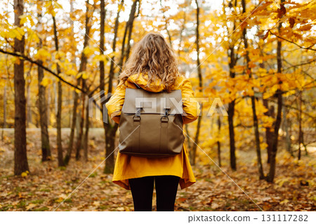 Back view. Curly woman with backpack in autumn forest enjoying nature. Concept of relaxation, nature 131117282