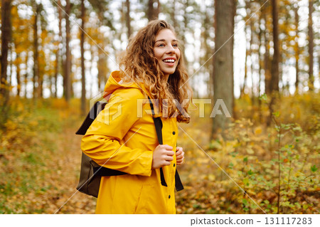 Hiking in autumn forest. Smiling tourist in bright coat walks through autumn park in sunny weather. 131117283