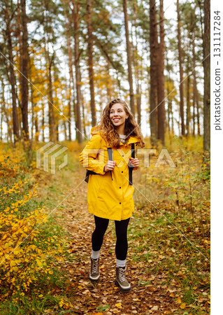 Hiking in autumn forest. Smiling tourist in bright coat walks through autumn park in sunny weather. 131117284