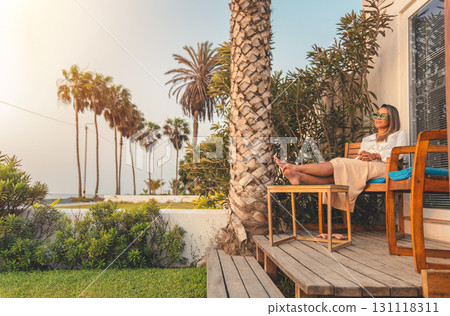 A woman is sitting on a wooden bench outside of a house beach A woman is sitting on a wooden bench outside of a house beach 131118311