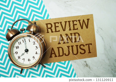 Review And Adjust text written on paper card with alarm clock on marble background 131120911