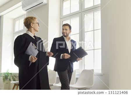 Judge woman in professional outfit black robe and man magistrate walk talking on judiciary documents 131121406