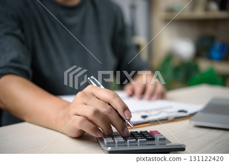 Close-up of hand using calculator for financial planning. Budget calculation, accounting report, and business finance management on desk with paper document and pen. Close-up of hand using calculator for financial planning. Budget calculation, accounting report, and business finance management on desk with paper document and pen. 131122420