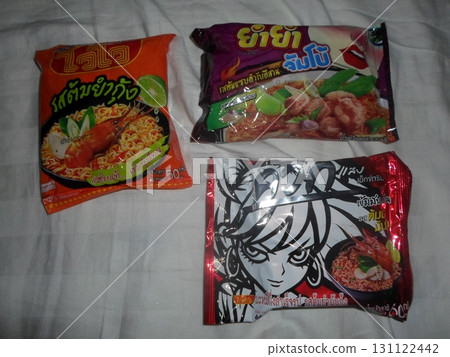Three Colorful Instant Noodle Packets with Different Flavors Displayed on a White Bed 131122442