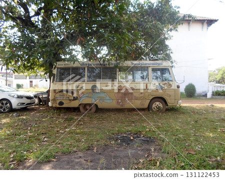 An Old Painted Bus Parked in a Grassy Yard Under a Tree with a House in the Distance 131122453