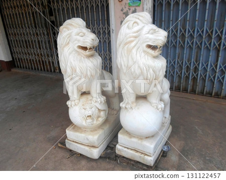 Two White Lion Statues Guarding a Metal Gate with Intricate Designs on a Concrete Base 131122457