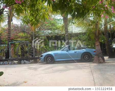 A Light Blue Convertible Parked in a Tropical Garden with Palm Trees and a Wagon Wheel A Light Blue Convertible Parked in a Tropical Garden with Palm Trees and a Wagon Wheel 131122458