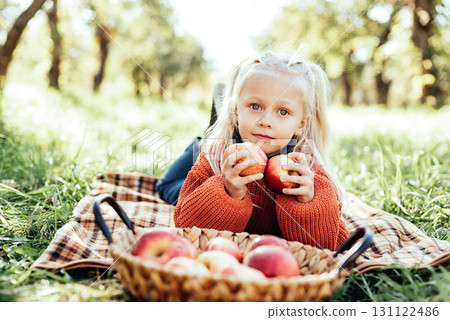 Child picking apples on farm in autumn. Little girl playing in tree orchard. Healthy nutrition. Cute little girl eating red delicious fruit. Harvest Concept. Apple picking. 131122486