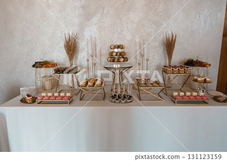 Elegant Dessert Table Setup with Gold Accents, Macarons, Fruits and Candles, Luxurious Event Decor, Neutral Beige Tones Elegant Dessert Table Setup with Gold Accents, Macarons, Fruits and Candles, Luxurious Event Decor, Neutral Beige Tones 131123159