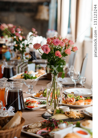 Elegant Wedding Reception Table Setting with Pink Roses. Food Platters, Glassware, and Rustic Decor in Warm Lighting 131123244