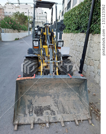 A mini excavator is parked on a narrow street in a residential neighborhood. The machine is ready for digging and construction tasks in the area. 131123362