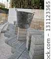 Workers are laying stone tiles in a pavement area, with a construction basket on top of stacked tiles. The setting suggests an ongoing outdoor construction project. 131123365