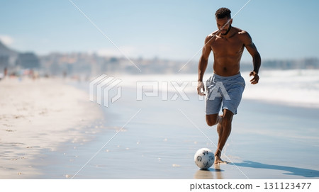 Man plays soccer on sandy beach during sunny day near ocean waves 131123477