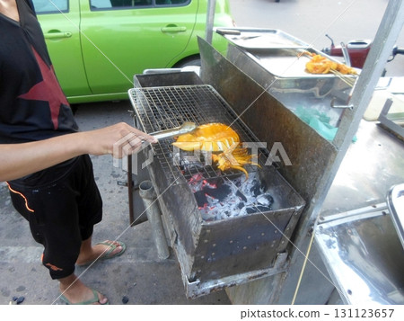 A Person Grilling a Large Squid on a Charcoal Grill at a Street Food Stand in the Day A Person Grilling a Large Squid on a Charcoal Grill at a Street Food Stand in the Day 131123657