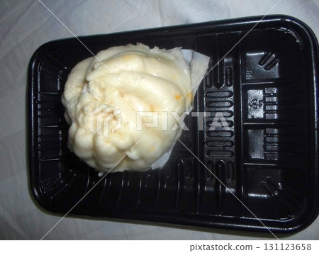 A Freshly Steamed Bun Resting in a Black Plastic Tray on a White Surface 131123658
