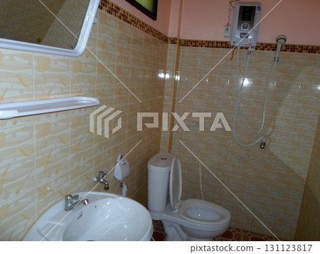 A Compact Tiled Tropical Bathroom with a Sink, Toilet, and Shower in a Warmly Lit Space 131123817