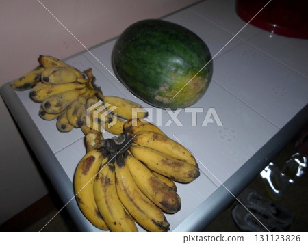 A Bunch of Ripe Bananas and a Whole Watermelon on a Tiled Table in a Tropical Kitchen Setting 131123826
