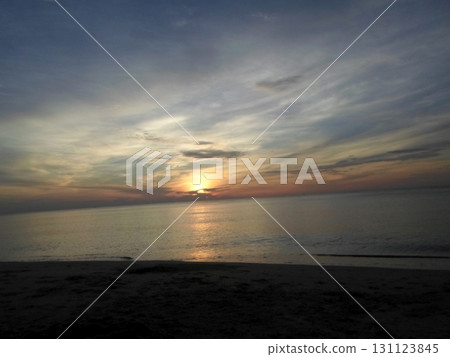 Sunset with Sun Touching Horizon Over Calm Ocean and Sandy Beach 131123845
