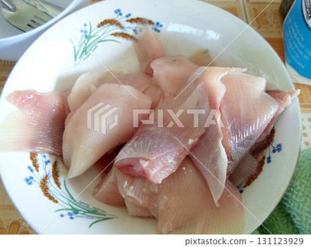 A Decorative Bowl Filled with Sliced Raw Fish on a Checkered Tablecloth with a Green Towel 131123929
