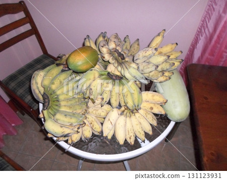 A White Basket Overflowing with Bananas, a Mango, and a Papaya in a Cozy Indoor Setting 131123931