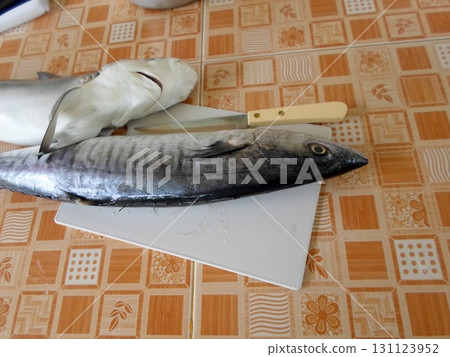 Fresh Fish on a Cutting Board with a Knife on a Patterned Table Surface 131123952