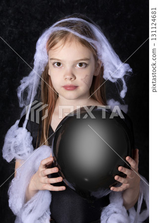 Little girl in a halloween spider web holding a black ball. 131124681