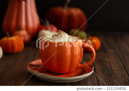 Cozy pumpkin latte in a pumpkin-shaped mug with whipped cream and spices, surrounded by autumn decor. Cozy pumpkin latte in a pumpkin-shaped mug with whipped cream and spices, surrounded by autumn decor. 131124830
