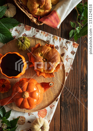 Autumnal tea set with pumpkin-shaped teapot and mug, and a baked bun on a wooden table. Top view. Copy space 131124838