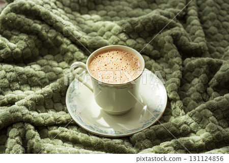 Frothy Coffee in Floral Cup on Cozy Green Blanket Frothy Coffee in Floral Cup on Cozy Green Blanket 131124856