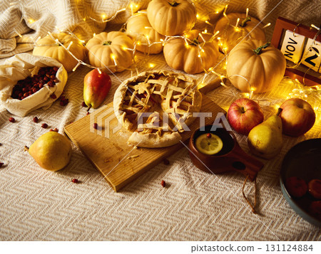 Cozy Thanksgiving Table Scene With Pumpkin Pie, Apples, Pears, and Lantern Lights Cozy Thanksgiving Table Scene With Pumpkin Pie, Apples, Pears, and Lantern Lights 131124884