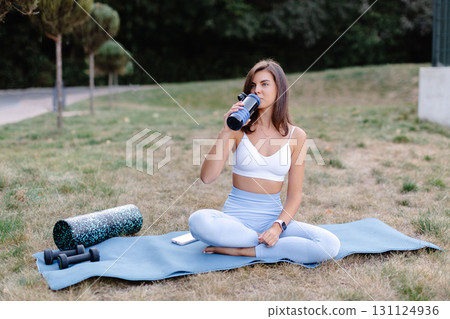 Young woman drinking water after outdoor workout in the park 131124936