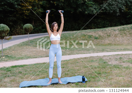 Young woman lifting weights during outdoor workout in a park Young woman lifting weights during outdoor workout in a park 131124944