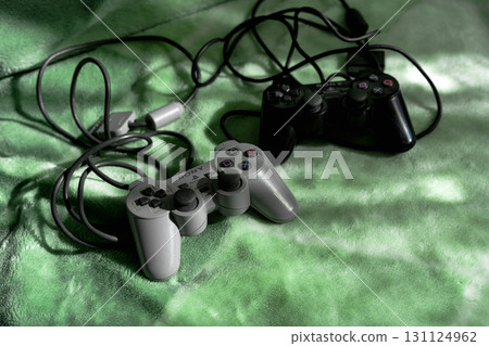 19 September 2025, Wroclaw Poland. Two PlayStation Dual Shock controllers grey and black version lie on a blanket, illuminated by the morning light. Nostalgic photo. 19 September 2025, Wroclaw Poland. Two PlayStation Dual Shock controllers grey and black version lie on a blanket, illuminated by the morning light. Nostalgic photo. 131124962