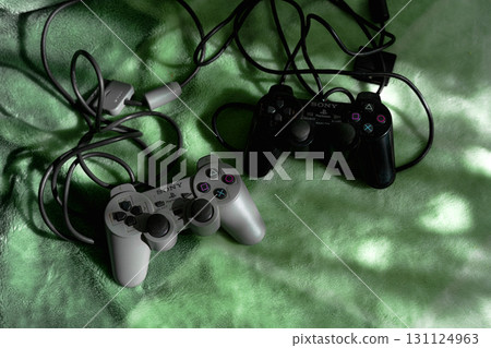 19  September 2025, Wroclaw Poland. Two PlayStation Dual Shock controllers grey and black version lie on a blanket, illuminated by the morning light. Nostalgic photo. 131124963