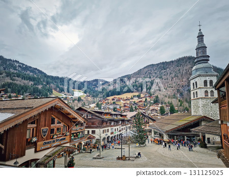 La Clusaz, Annecy, France - February 10, 2024 Picturesque village with traditional wooden chalets nestled in the valley, surrounded by forested french Alps mountains. Winter holidays season 131125025